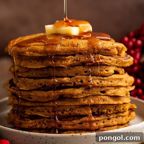 Tall stack of golden gingerbread pancakes with maple syrup being drizzled from above with butter on top