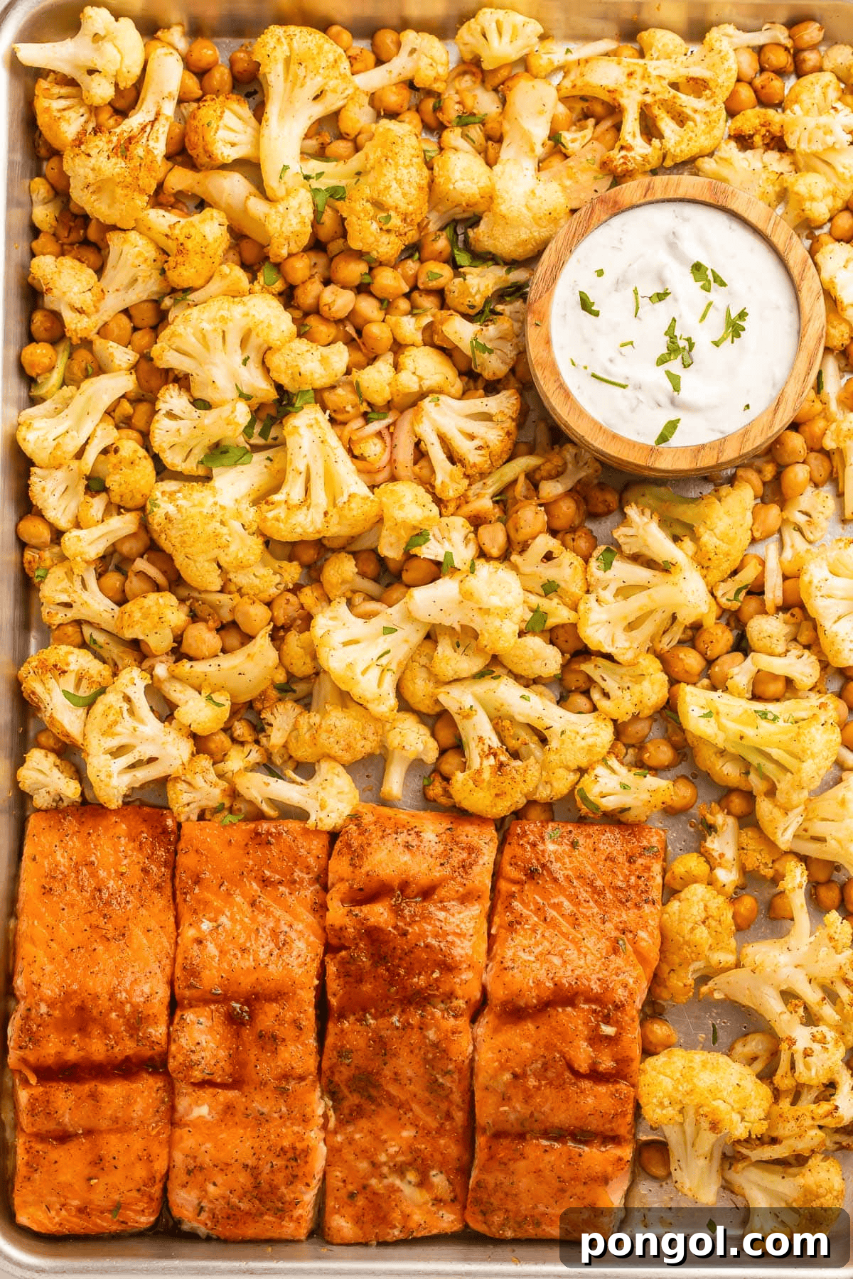 Sheet pan salmon dinner with roasted cauliflower, shallots, and garbanzo beans, drizzled with hot honey and cilantro-lemon yogurt sauce