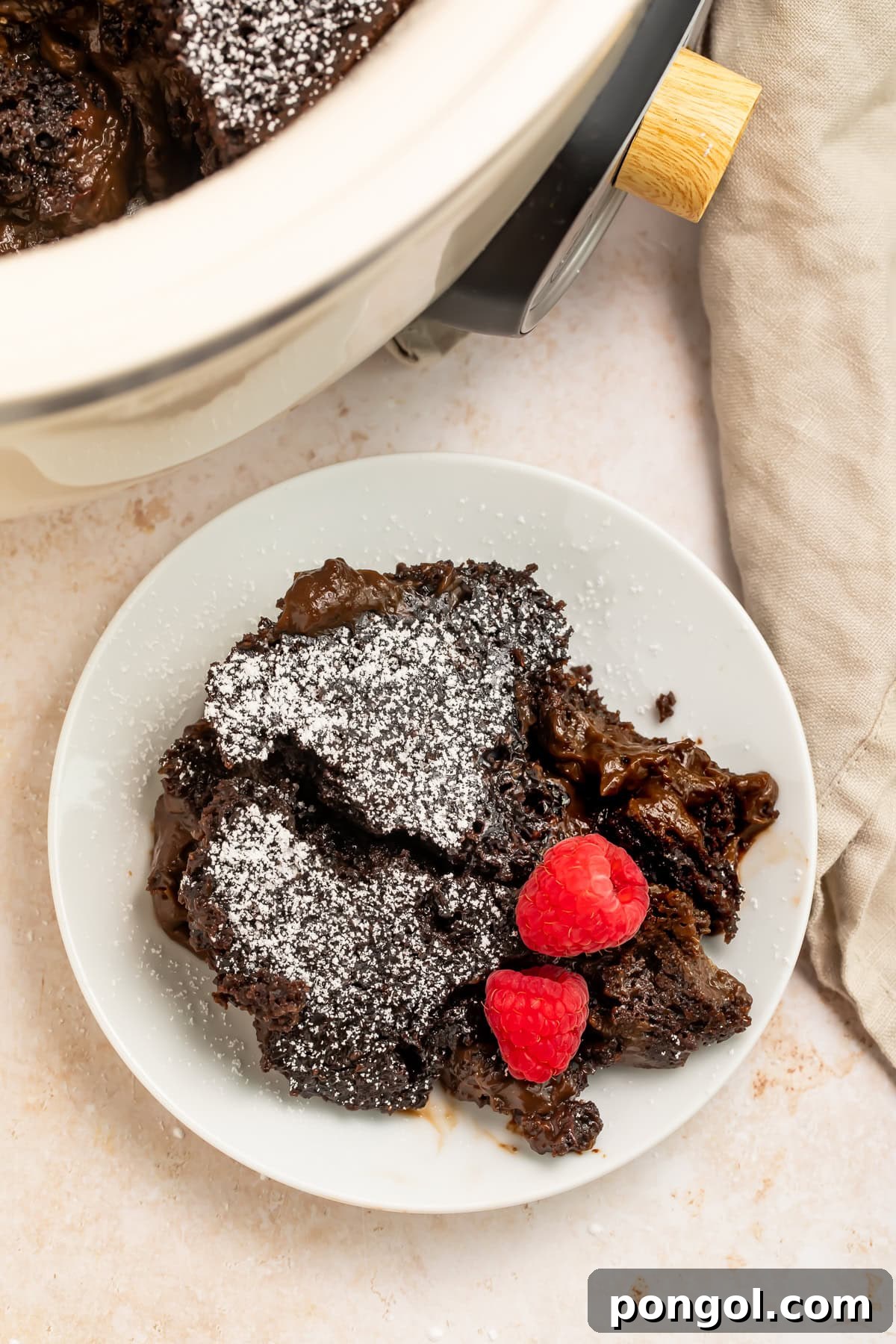 A delectable slow cooker molten lava cake, garnished with powdered sugar and fresh raspberries, served on a pristine white plate.