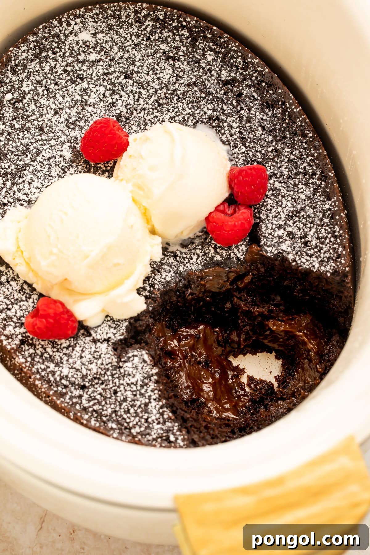 Overhead view of slow cooker molten lava cake served with vanilla ice cream and fresh raspberries.