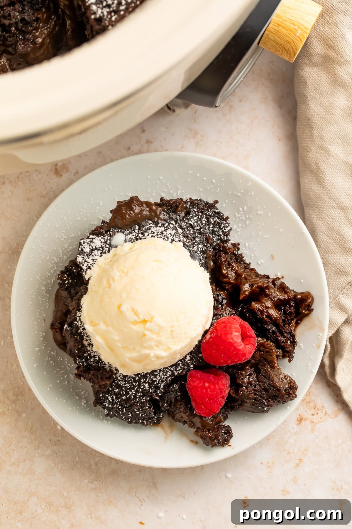 Slow cooker lava cake with vanilla ice cream and raspberries dusted with powdered sugar, ready to be enjoyed.