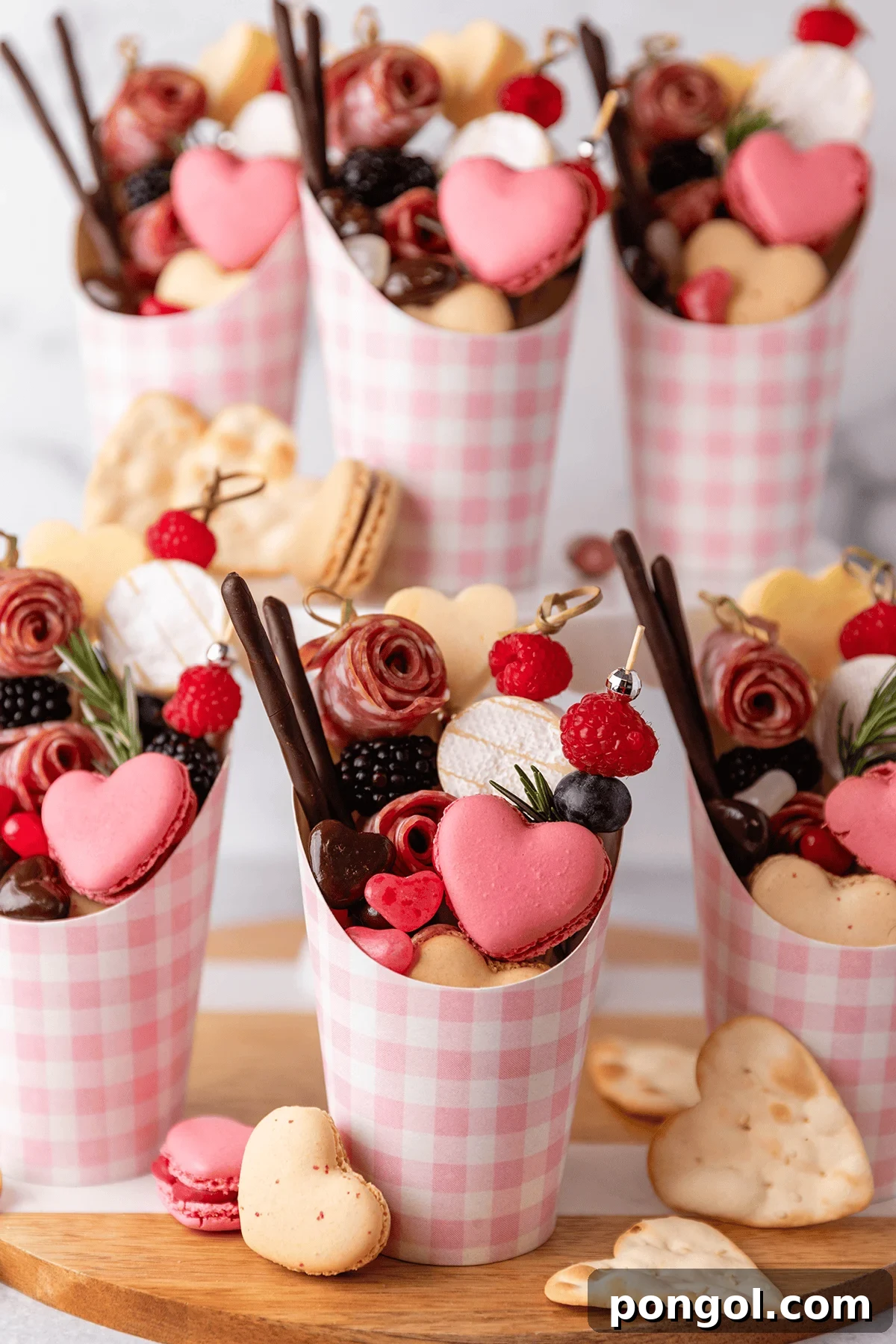 Beautifully arranged individual pink-themed charcuterie cups for a Galentine's celebration, featuring salami roses, cheeses, crackers, fruits, and chocolates
