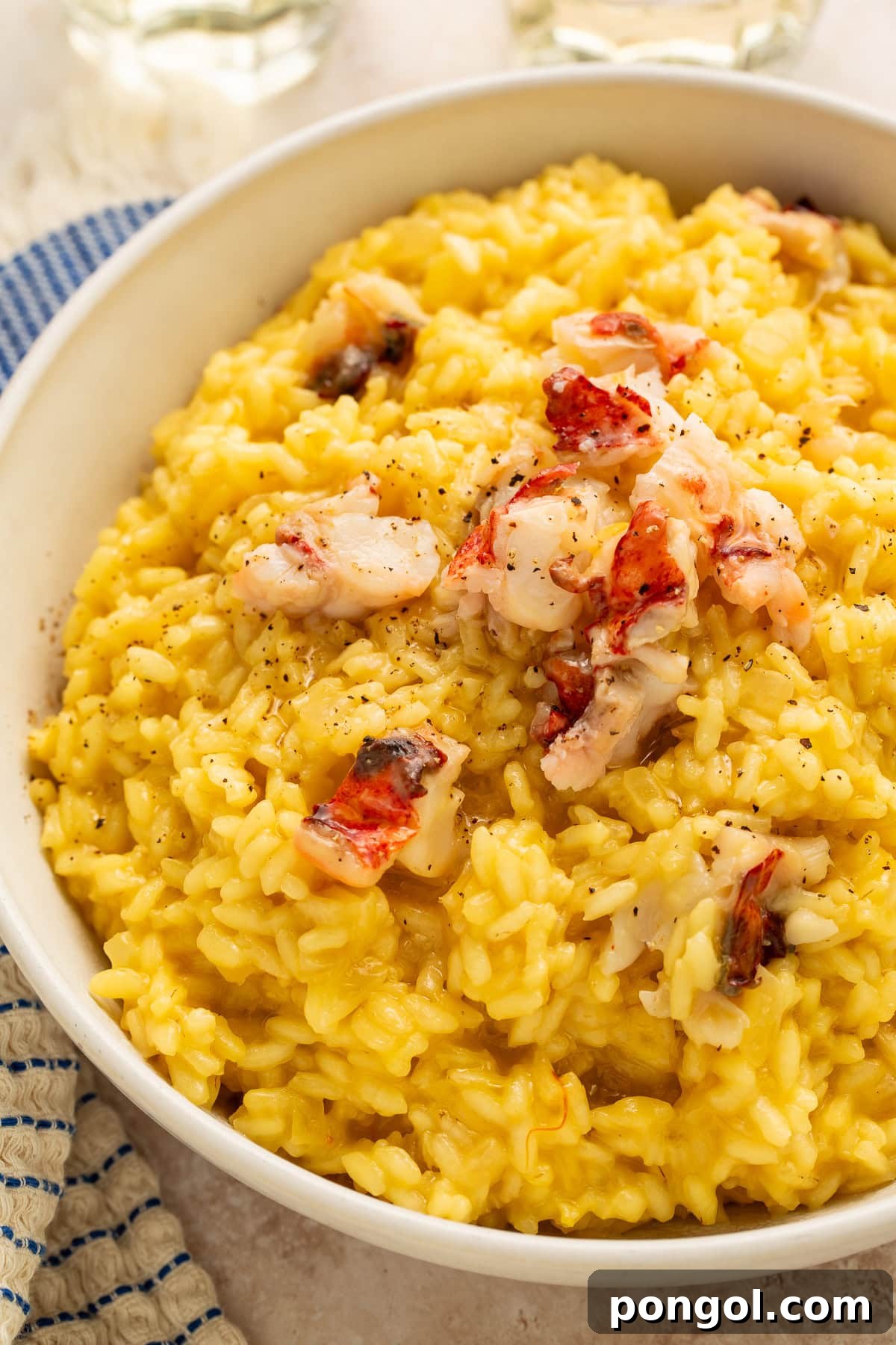 Creamy golden lobster risotto, elegantly topped with succulent butter-poached lobster chunks and a sprinkle of black pepper, served in a pristine white bowl