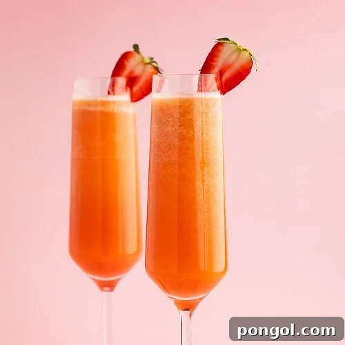 Two strawberry mimosas in champagne flutes garnished with halved strawberries on a pink background