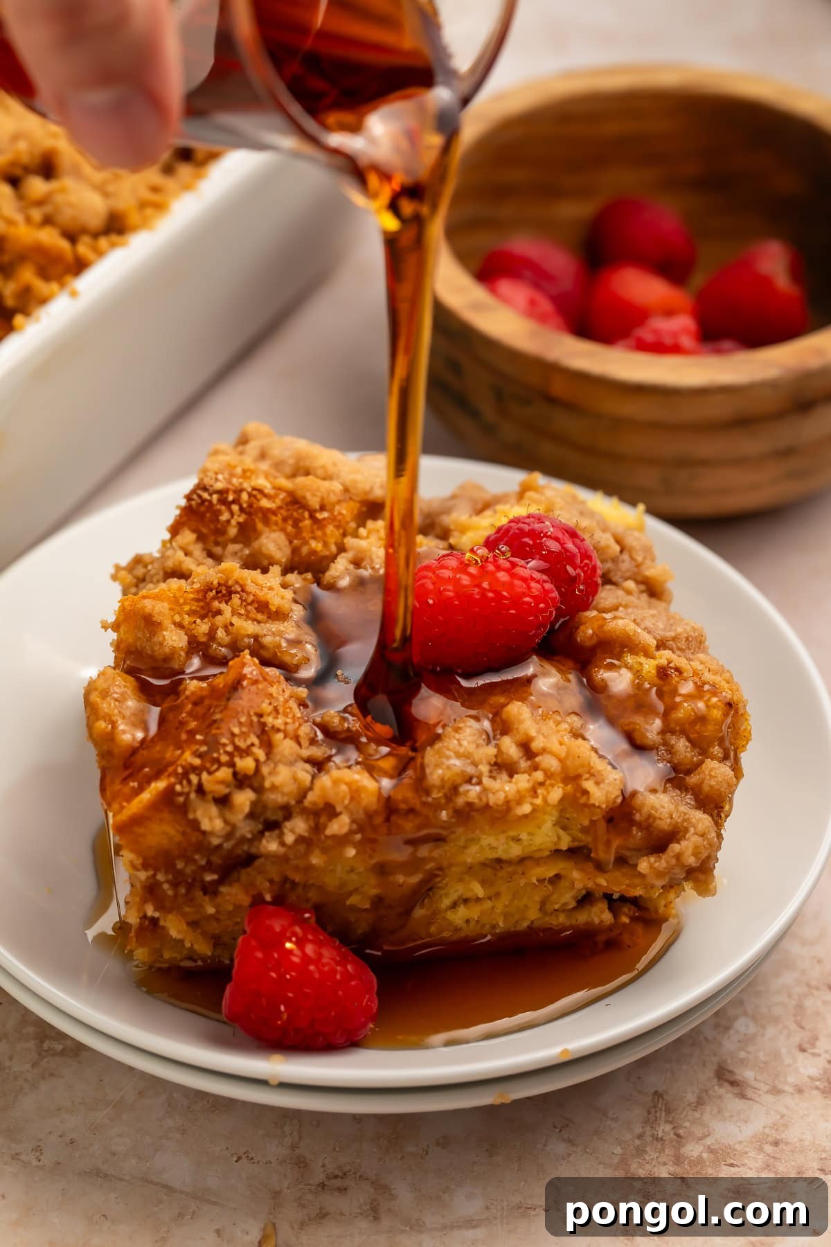Easter Feasts Gifts and Fun Your Complete Celebration Guide 7 Maple syrup pouring over a slice of brioche French toast casserole with raspberries on a white plate, a decadent Easter brunch dish.