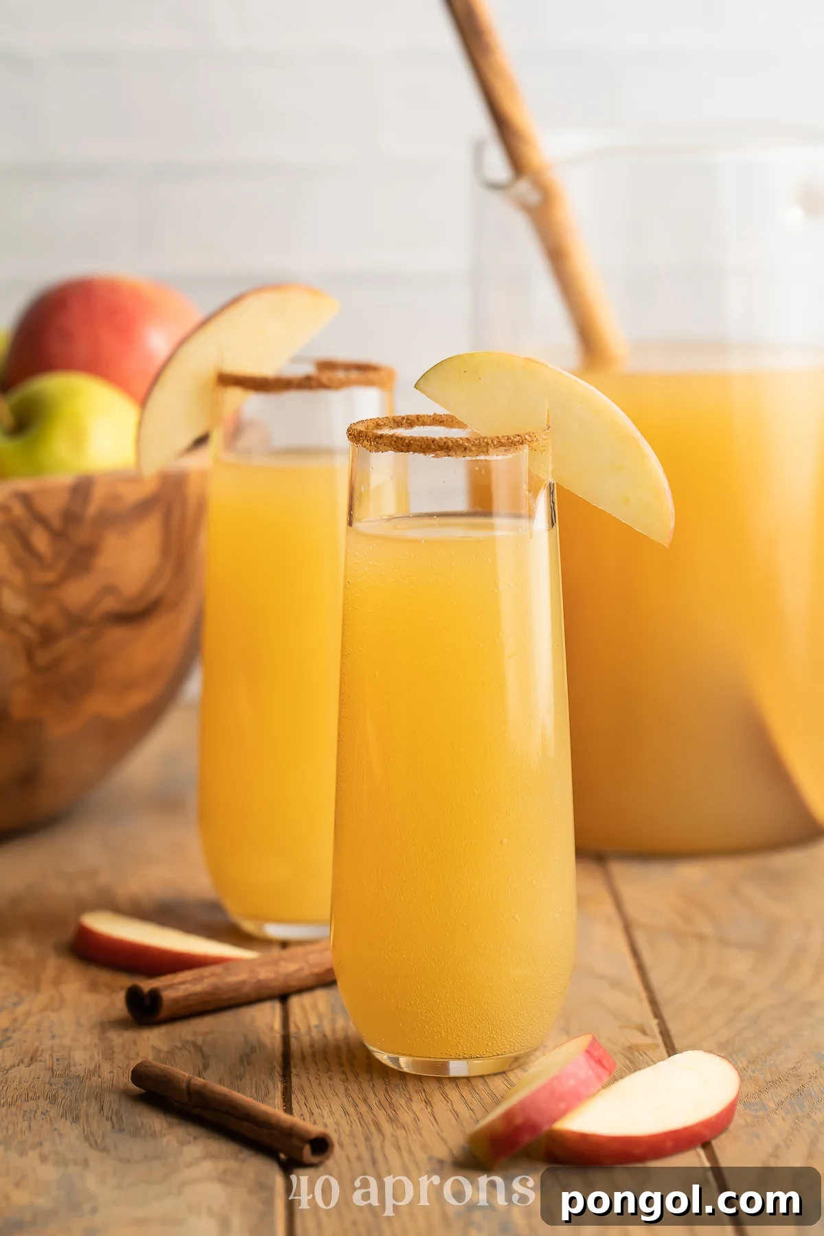 Zoomed out photo of two mimosas glasses holding apple cider mimosas rimmed with brown sugar cinnamon sitting in front of a bowl of apples.