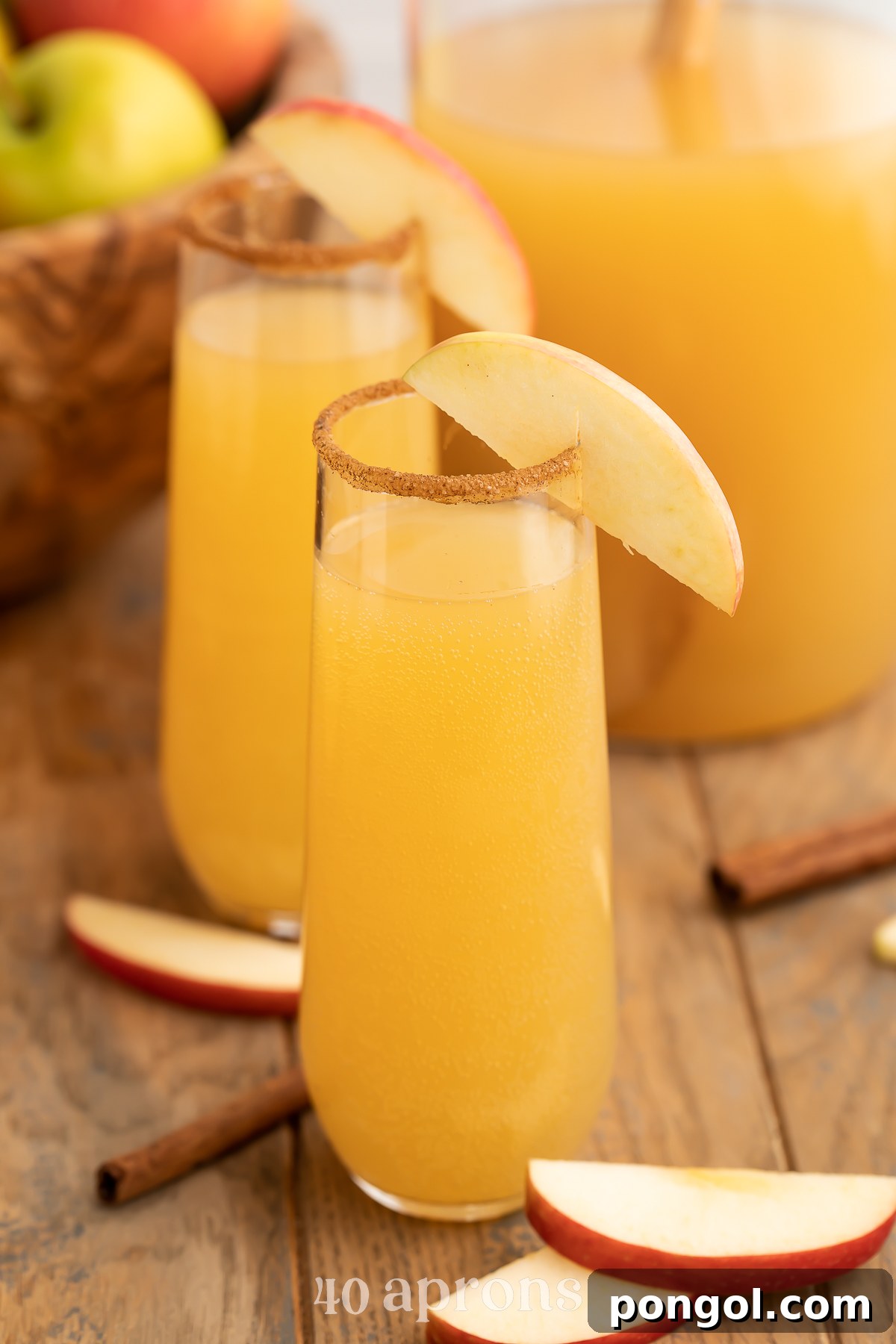 Two apple cider mimosas in stemless champagne flutes rimmed with cinnamon sugar and garnish with apple wedges.