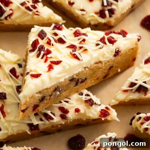 Triangular cranberry bliss bars topped with cranberries and cream cheese frosting.