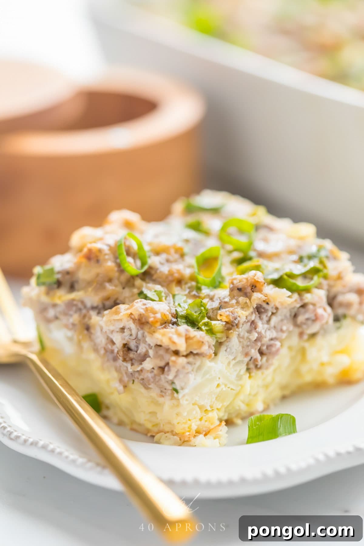 A square of Whole30 hashbrown sausage casserole on a plate with a gold fork.