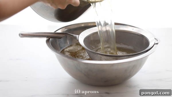 Strained bone broth through a mesh strainer over a silver bowl