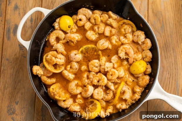Big Easy BBQ Shrimp Po Boy 5 Overhead view of buttery BBQ shimp in a large skillet with lemon slices.