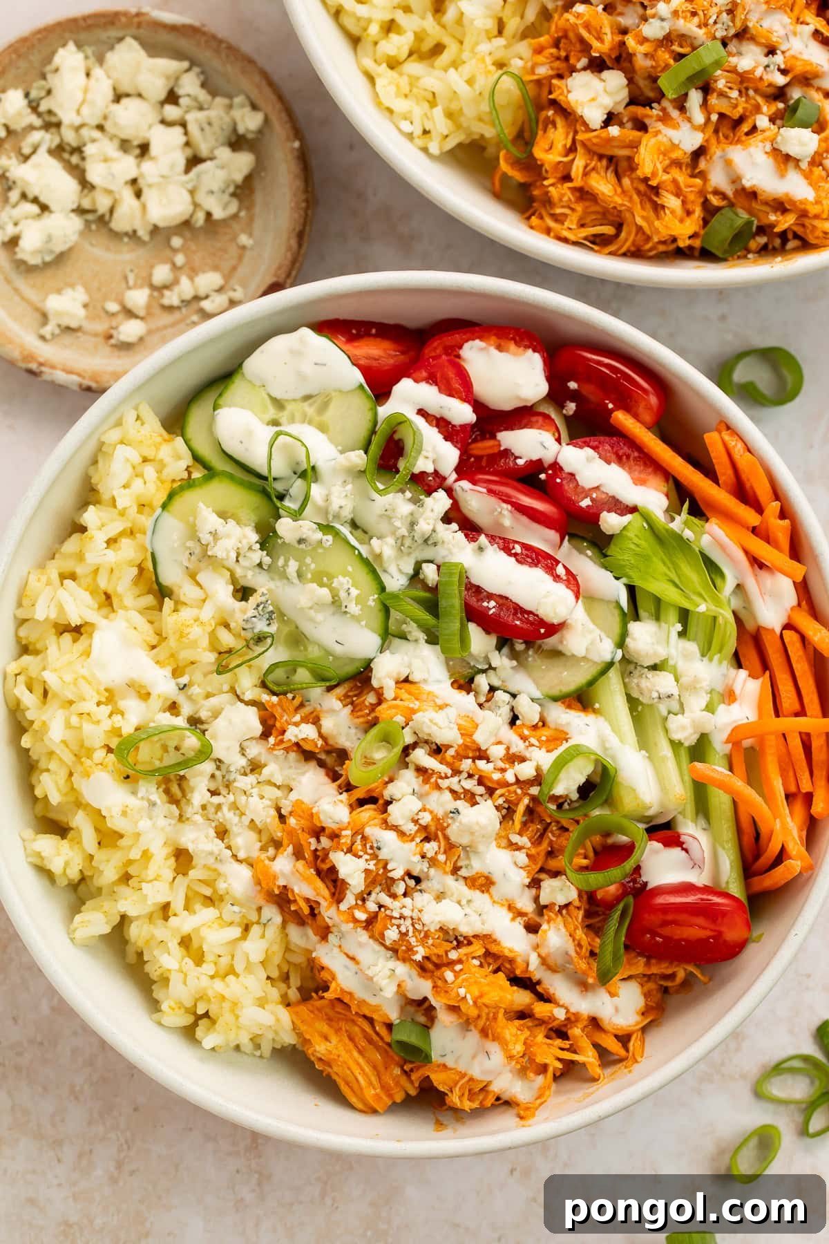 buffalo chicken bowls with shredded chicken, rice, fresh vegetables, and blue cheese crumbles in white bowls