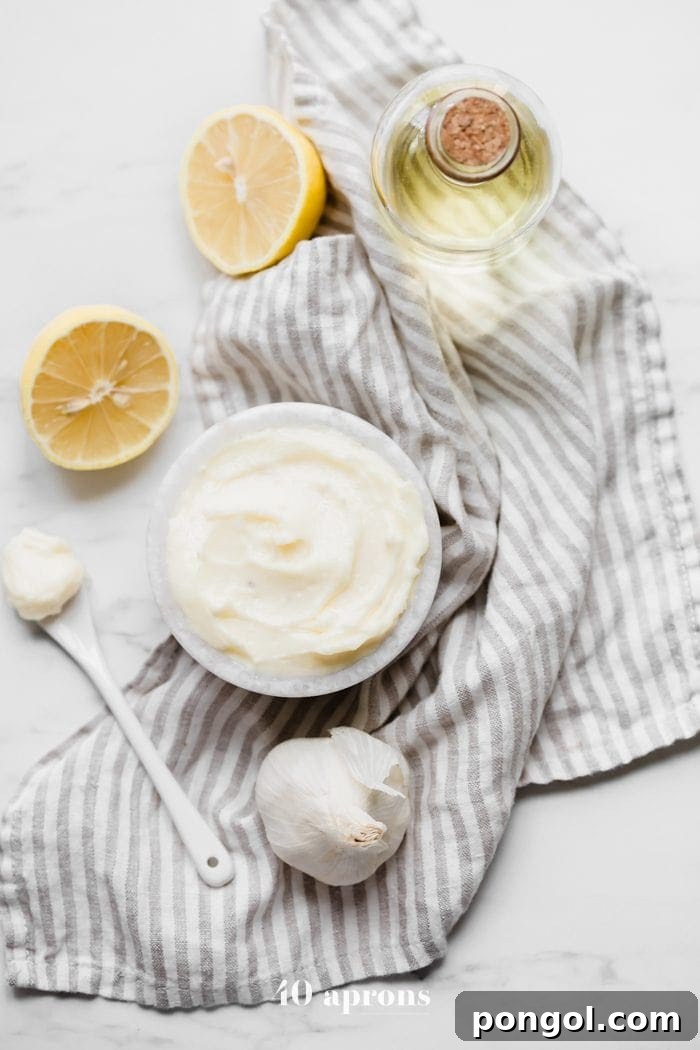 Delicious Whole30 coconut oil mayonnaise in a bowl, surrounded by fresh lemons, garlic cloves, and a bottle of coconut oil.