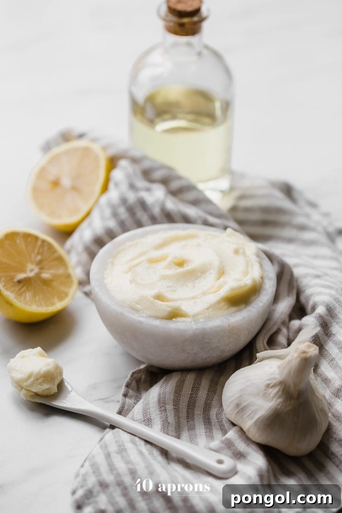 A close-up of Whole30 coconut oil mayonnaise in a bowl, garnished with lemon slices, garlic, and a decorative display of coconut oil.