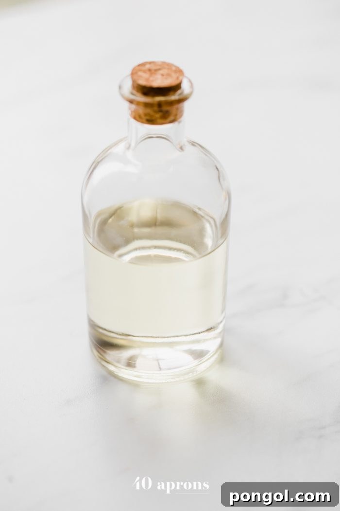 A glass jar with a cork stopper, filled with clear fractionated coconut oil (liquid coconut oil), highlighting its liquid state.