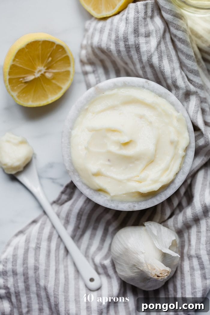 Fresh Whole30 coconut oil mayonnaise in a rustic bowl, accompanied by bright lemons, garlic cloves, and a small dish of coconut oil, set on a wooden surface.