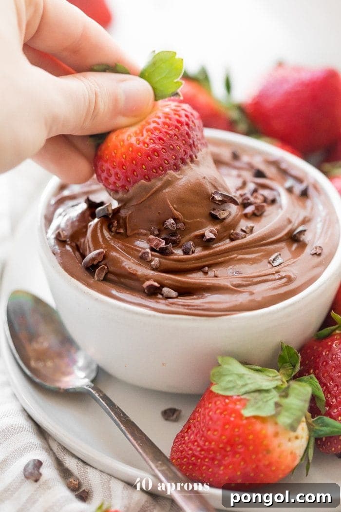 A rich, dark paleo chocolate mousse dip in a white bowl, surrounded by vibrant red strawberries, perfect for a healthy Valentine's Day treat. The dip is creamy and inviting, contrasting beautifully with the fresh fruit.