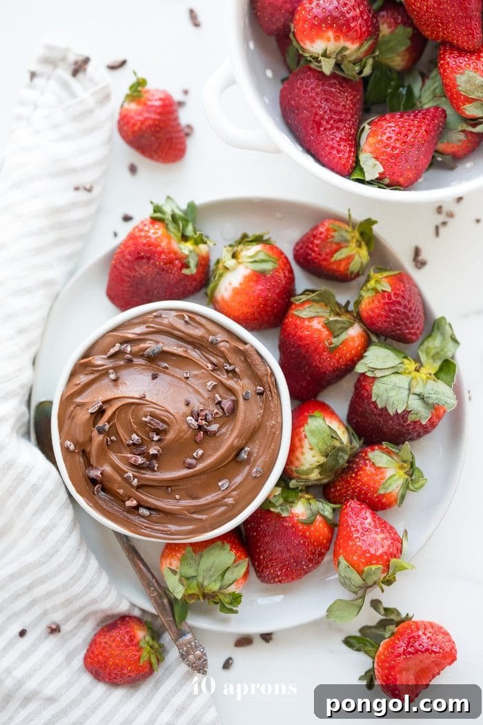 Overhead view of a spread featuring the paleo chocolate mousse dip, fresh strawberries, and other fruits arranged around the bowl, indicating a perfect dessert board component or healthy snack.