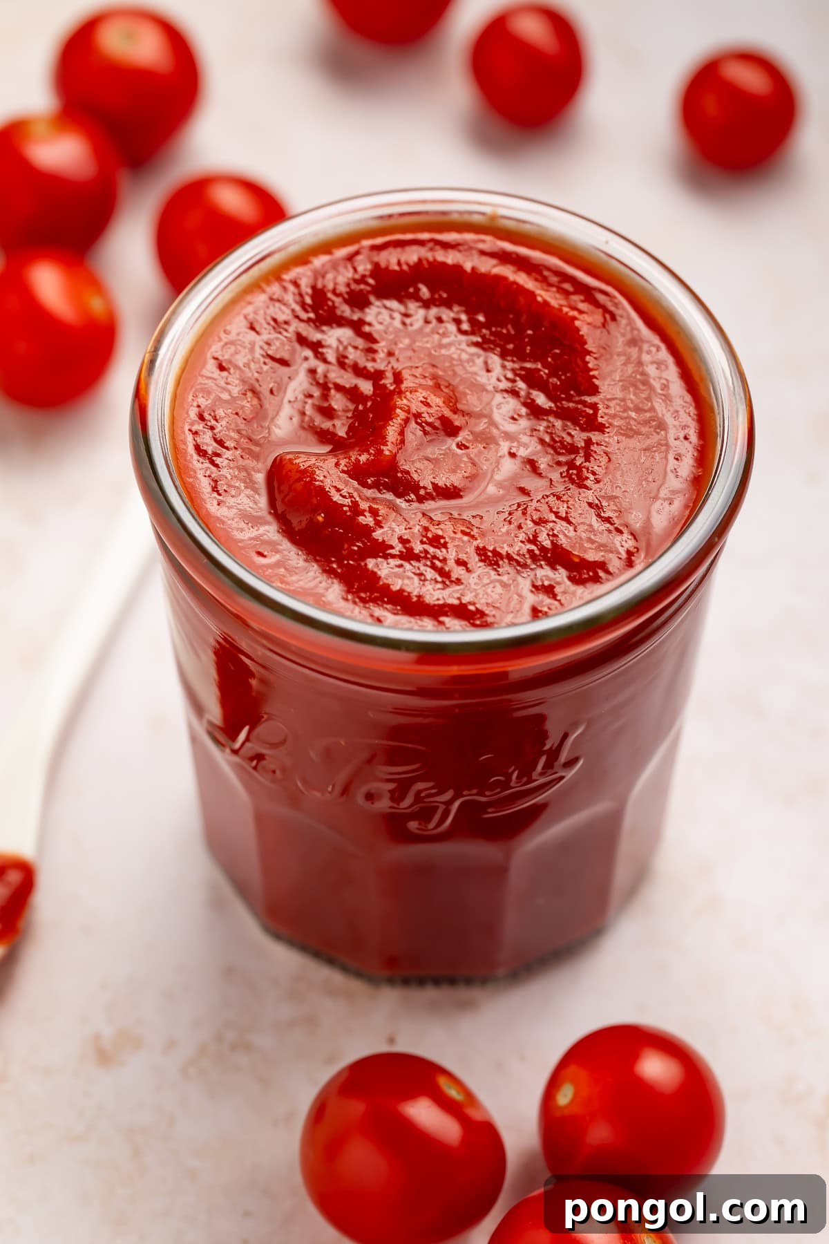 Jar of homemade tomato ketchup with cherry tomatoes scattered around.