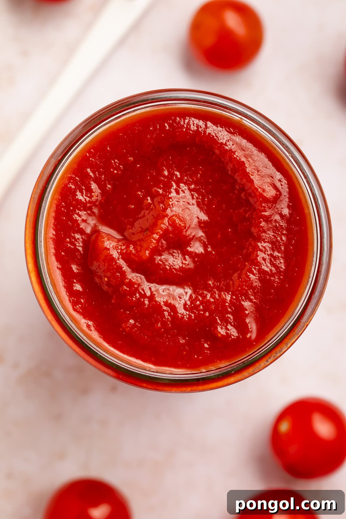 Overhead photo of homemade ketchup in a glass jar with grape tomatoes scattered around it on the countertop.