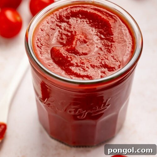Jar of homemade tomato ketchup with cherry tomatoes scattered around.