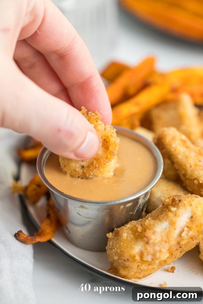 Hand dipping paleo Whole30 chicken nuggets into dipping sauce with sweet potato fries in background