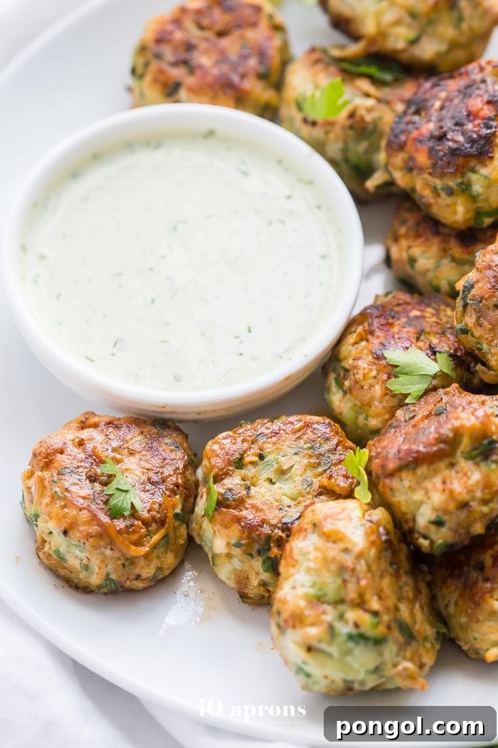 A plate of perfectly cooked Whole30 Chicken Bacon Ranch Poppers, highlighting the crispy bacon bits and green herbs, served with a bowl of creamy ranch.