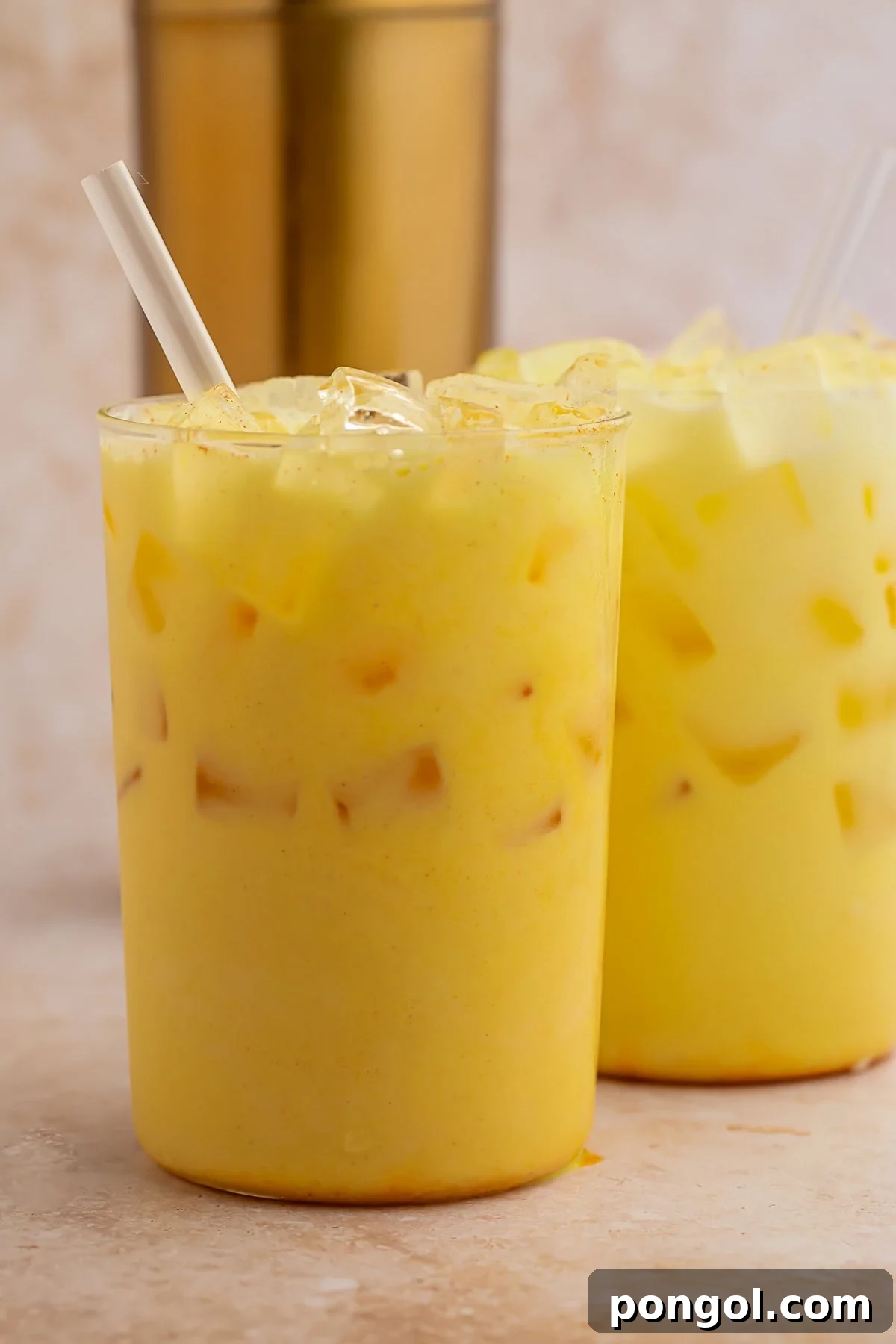 Two perfectly prepared Iced Golden Milk Lattes in glasses filled with ice, resting on a clean countertop, ready to be enjoyed.