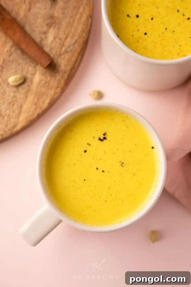 The drink served in mugs on a pink background, showcasing a warm golden milk.