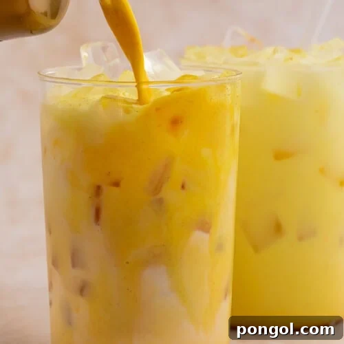 Iced golden milk latte being poured into a glass filled with ice.