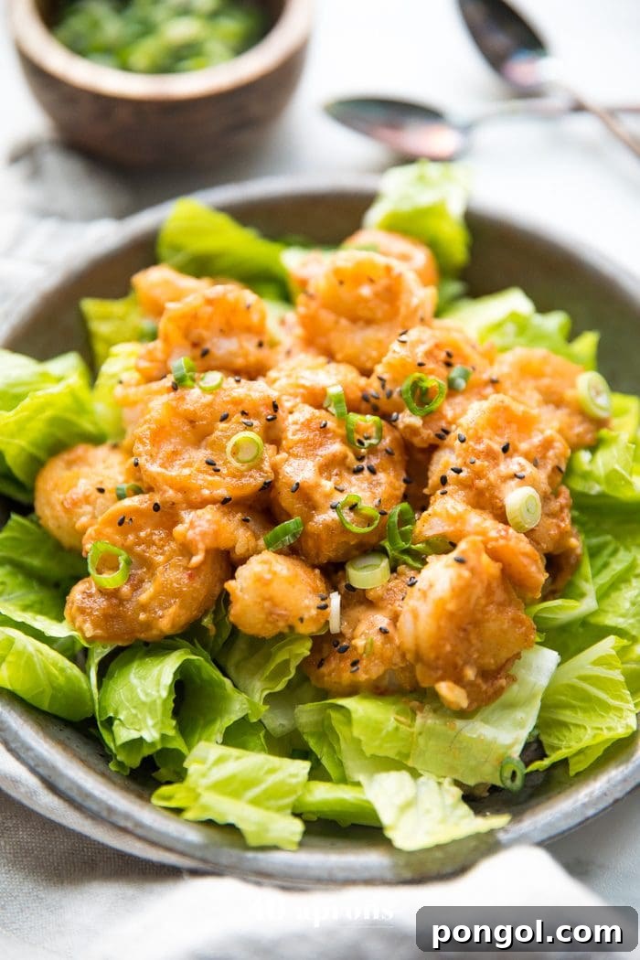 Whole30 bang bang shrimp on a bed of romaine lettuce with green onions and sesame seeds