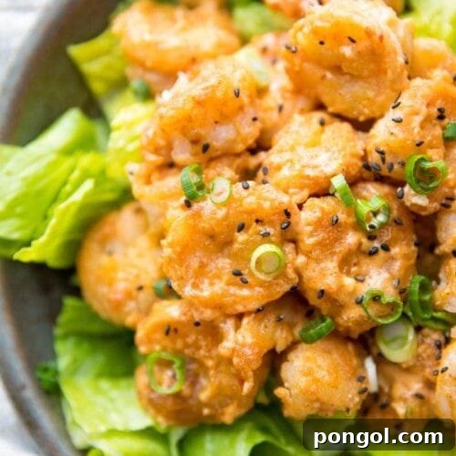Whole30 bang bang shrimp topped with green onions and sesame seeds on a bed of romaine lettuce