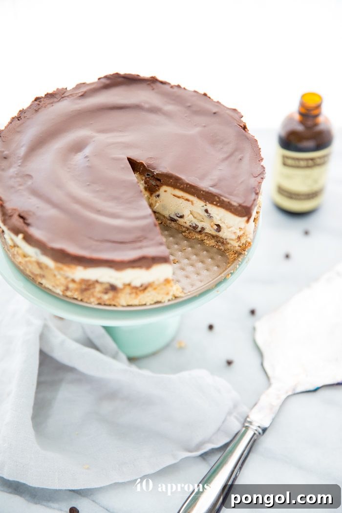Whole vegan no bake cookie dough cheesecake on a cake stand with a slice cut out, revealing the layers.