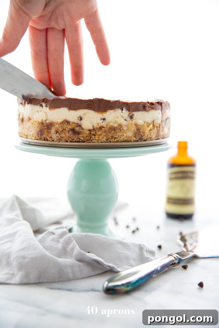 Hand cutting a slice of vegan no bake cookie dough cheesecake from a whole cake on a stand.