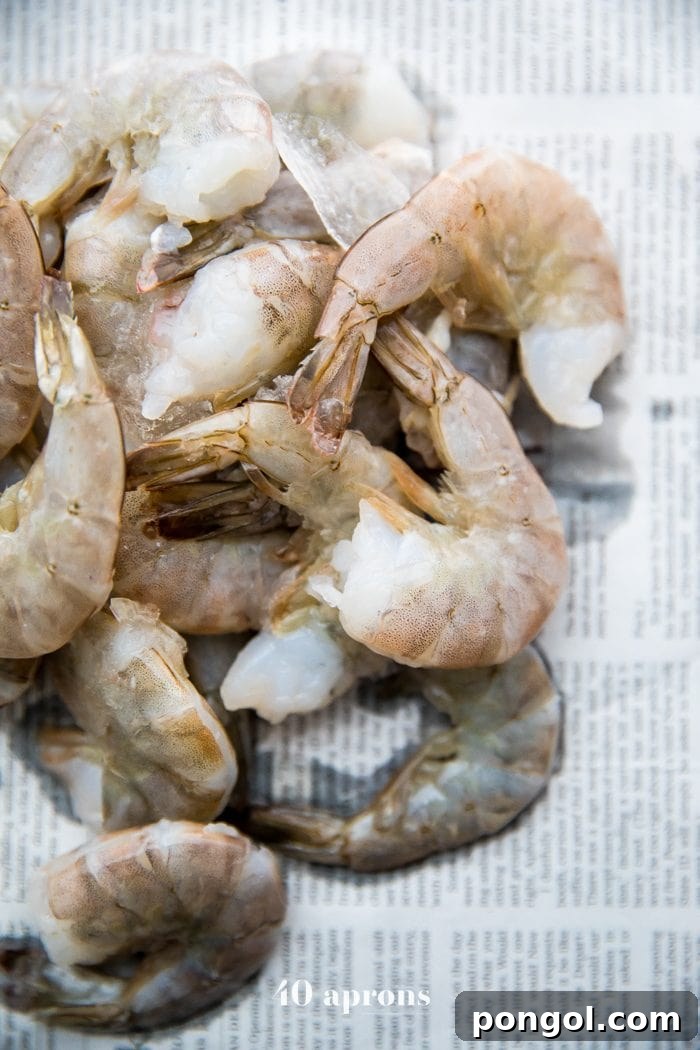 Whole30 Paleo Garlic Ghee Shrimp Boil with Sausage and Potatoes 4 Fresh, unpeeled shrimp ready for a Whole30 shrimp boil, artfully scattered on newspaper, highlighting the simplicity and casual charm of the dish