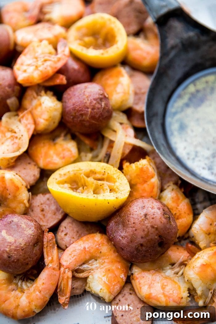 Whole30 Paleo Garlic Ghee Shrimp Boil with Sausage and Potatoes 7 A large serving of Whole30 shrimp boil, featuring shrimp, sausage, and potatoes, topped with fresh lemon slices and Old Bay seasoning, presented on newspaper