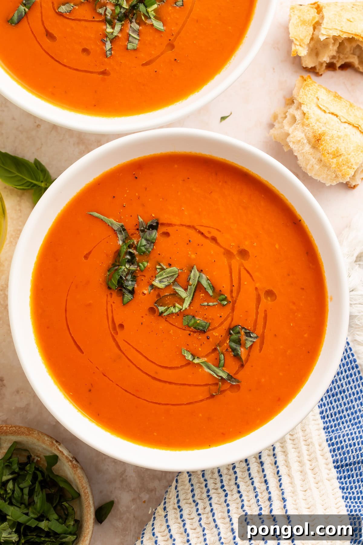Whole30 tomato soup in white bowls with fresh basil garnish and crusty bread on marble surface