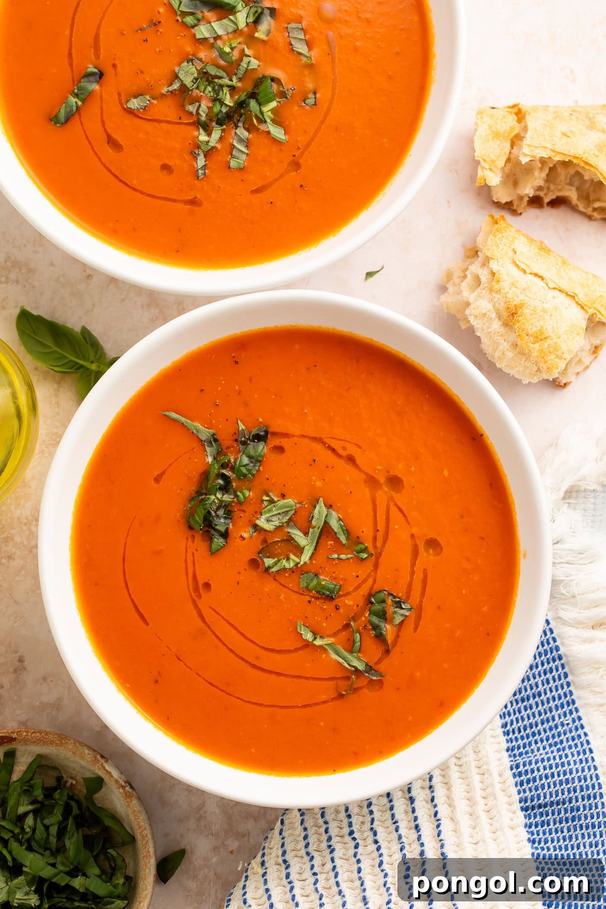 Whole30 tomato soup in white bowls with fresh basil garnish and crusty bread on marble surface