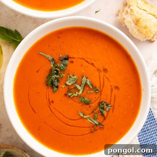 Whole30 tomato soup in white bowls with fresh basil garnish and crusty bread on marble surface