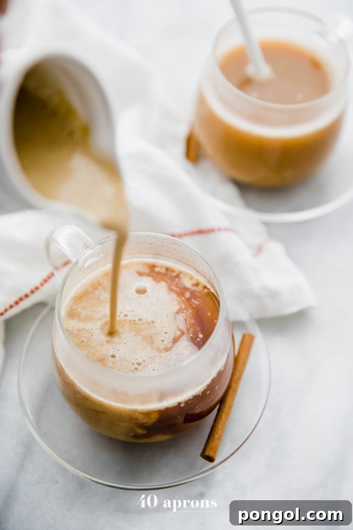 Whole30 pumpkin spice creamer in a jug pouring into a cup of coffee with a cinnamon stick and second cup of coffee in the background