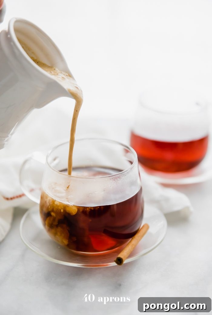 Whole30 pumpkin spice creamer in a jug pouring into a cup of coffee with a cinnamon stick and second cup of coffee in the background