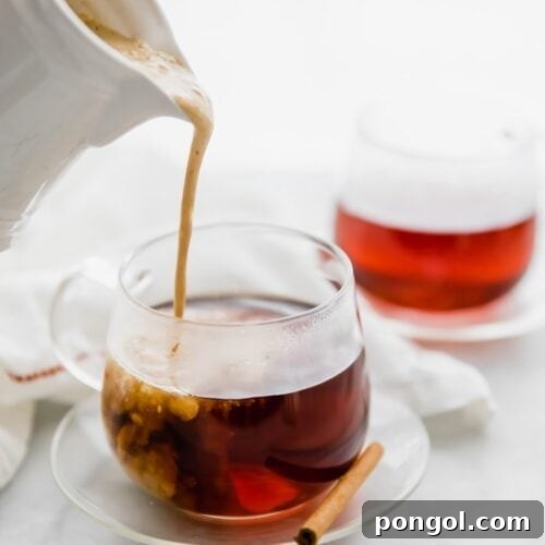 Whole30 pumpkin spice creamer in a jug pouring into a cup of coffee with a cinnamon stick and second cup of coffee in the background