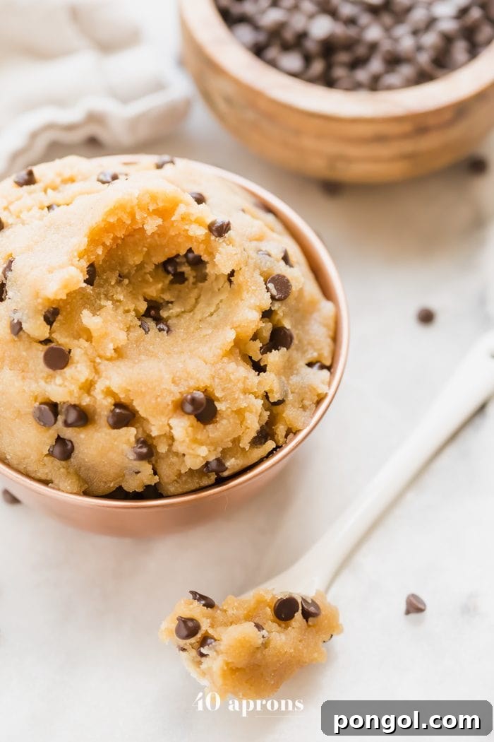 Vegan healthy cookie dough in a copper bowl with a bite taken out and a bowl of chocolate chips in the corner