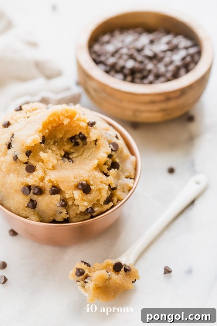 Vegan healthy cookie dough in a copper bowl with a bite taken out and a bowl of chocolate chips in the corner