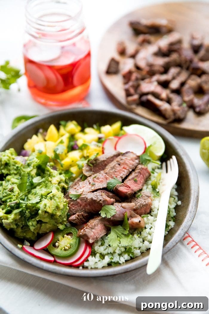 Healthy Steak Taco Bowls with vibrant pineapple salsa, creamy avocado, and fresh radishes on cauliflower rice.
