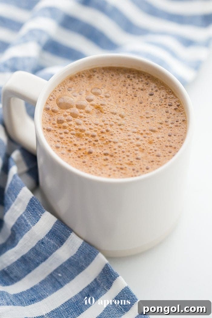 A steaming mug of golden miracle maca latte, placed on a wooden surface next to a blue-striped towel, inviting warmth and comfort