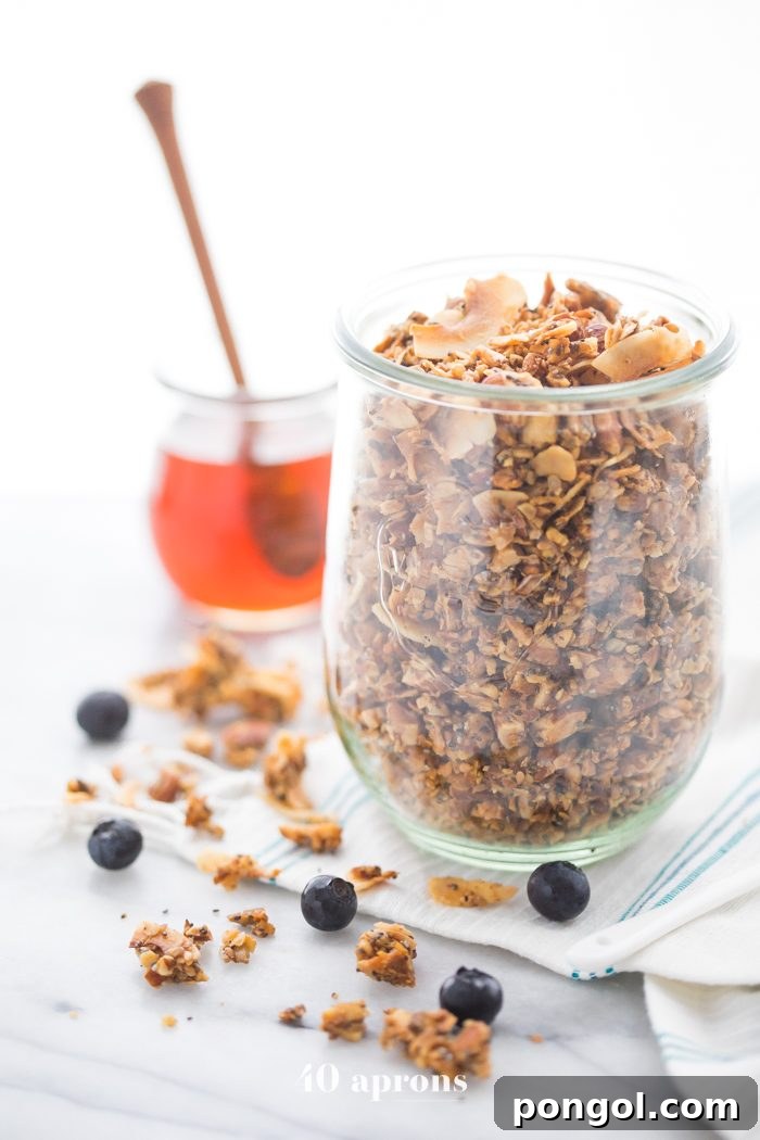 A glass jar of a crunchy paleo granola recipe with a jar of honey in the background