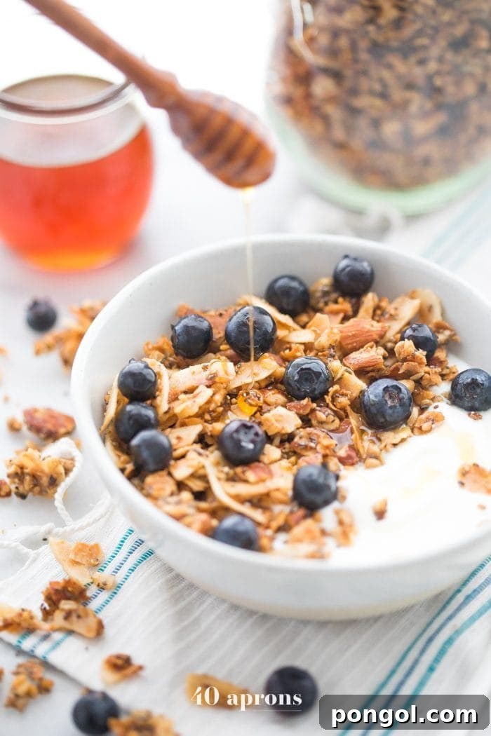 Bowl of the crunchy paleo granola recipe over yogurt, topped with blueberries and a drizzle of honey