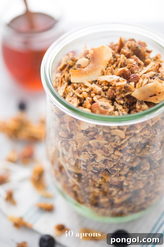 A glass jar of a crunchy paleo granola recipe with a jar of honey in the background