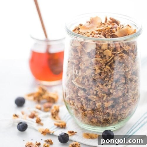 A glass jar of a crunchy paleo granola recipe with a jar of honey in the background
